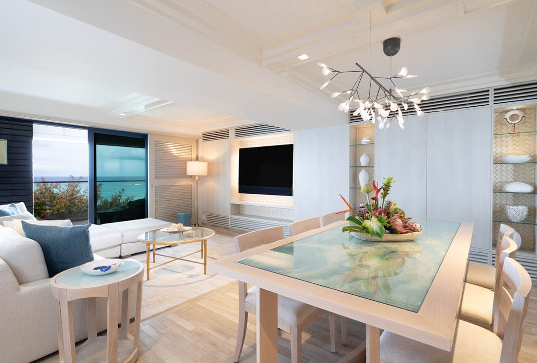Dining area with table, chairs, and living area with TV, couch, balcony with ocean view.